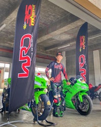 a man standing next to two green motorcycles