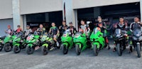 a group of people posing in front of a garage with green motorcycles