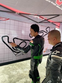 two motorcyclists standing next to a map of a track